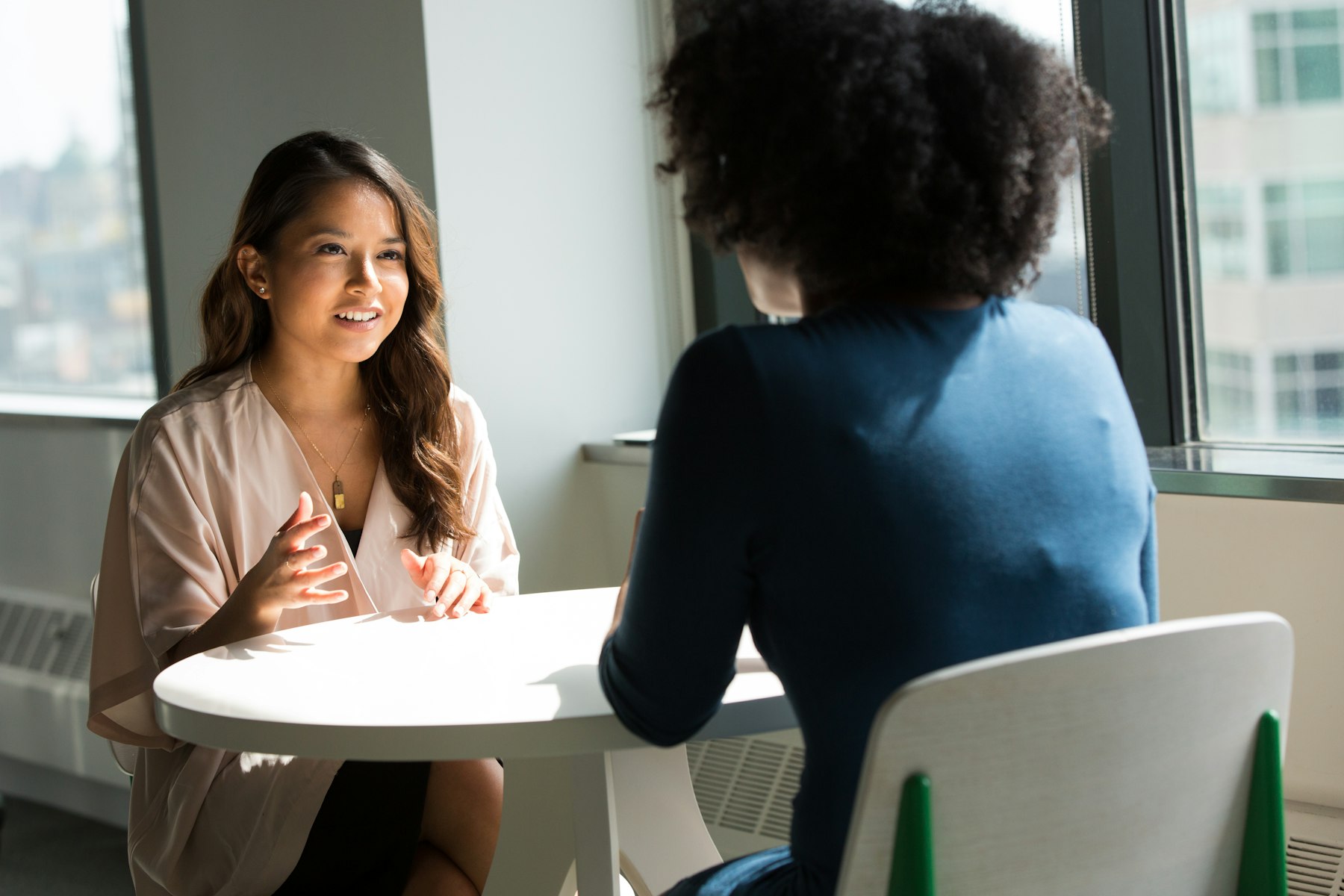 Two colleagues talking across a table beside a window